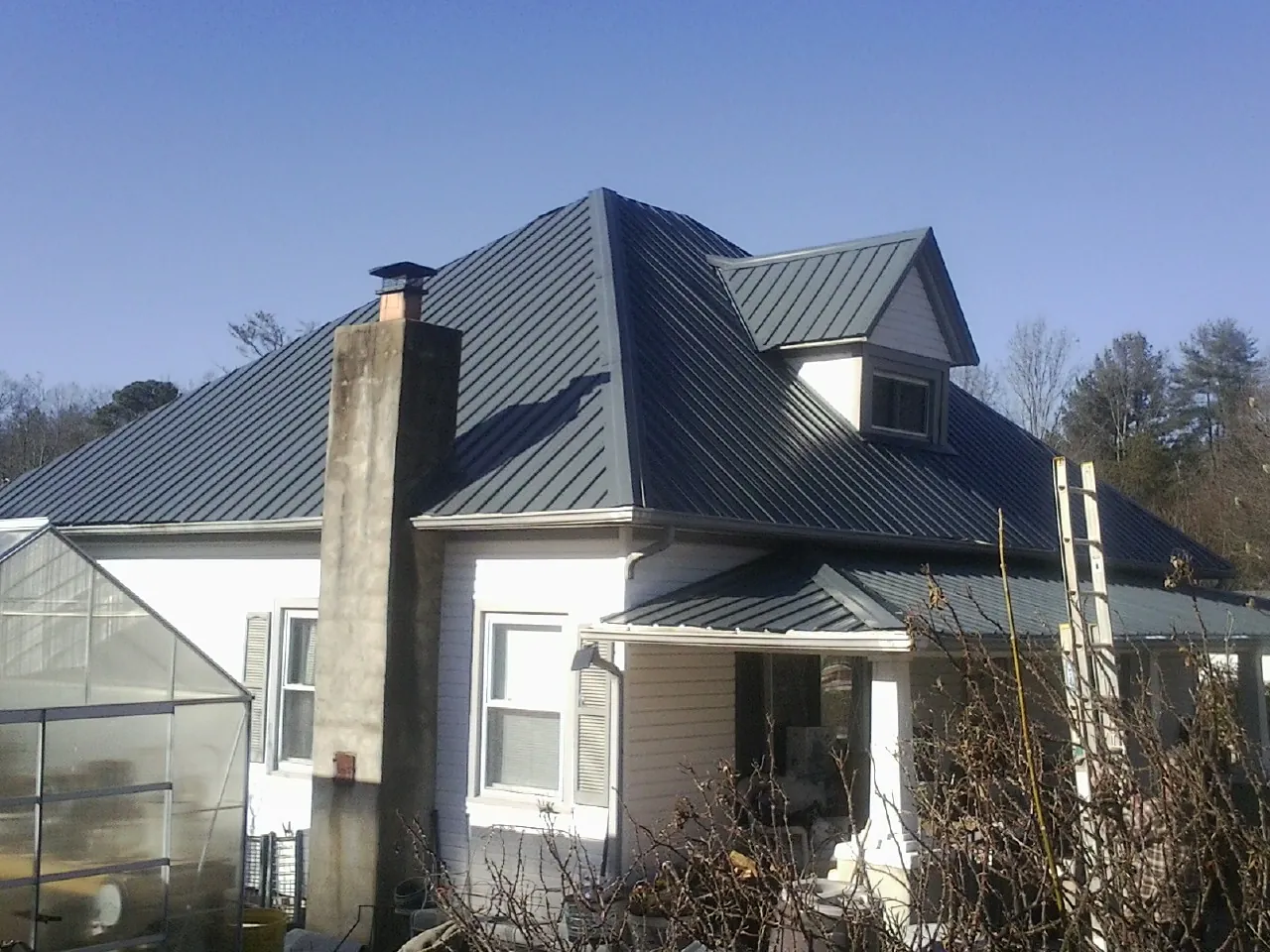 Dark blue standing seam metal roof on a white farmhouse with dormer — Slate & Tile Roof Repair by Roofing Brothers in Matthews