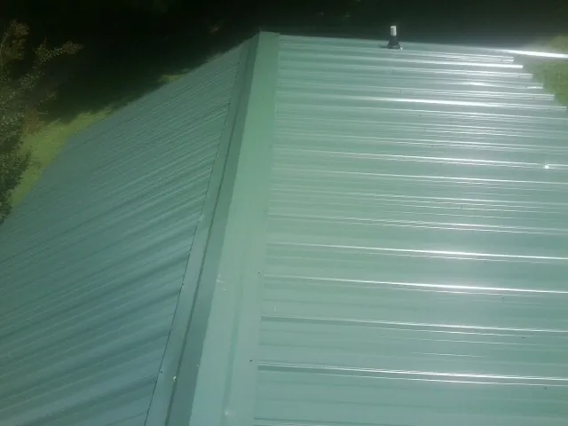 New green metal panels meeting at the ridge of a roof — Flat Roof Repair work by our crew in Matthews